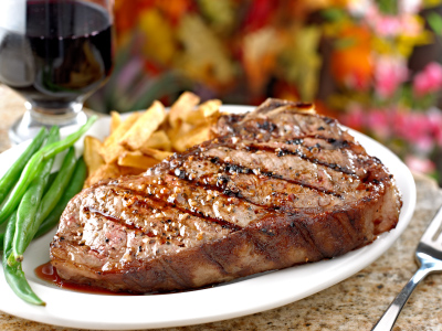 Grilled steak with french fries and green beans on a white a plate, sitting on a granite table.